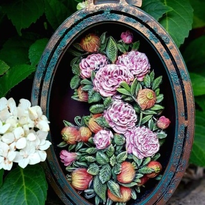 Moldura oval envelhecida com ilustração de flores rosas e pêssegos em fundo escuro, em ambiente natural com folhagem e flores brancas
