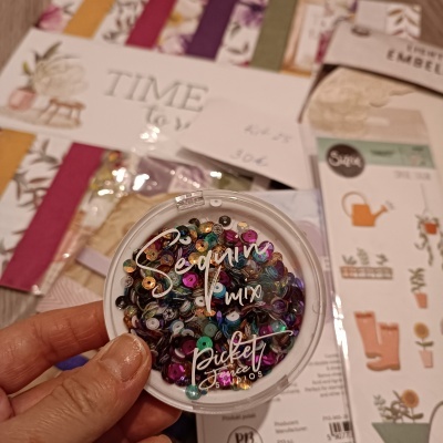 Embalagem redonda com lantejoulas multicoloridas e papéis decorativos ao fundo