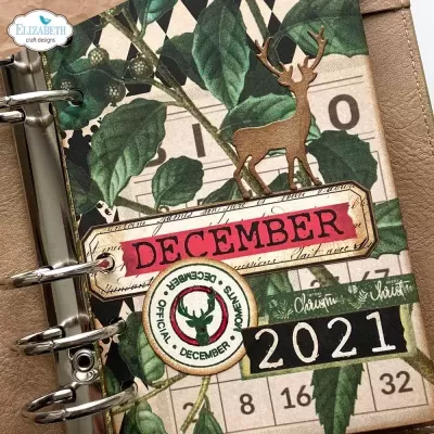 Agenda decorada com folhas verdes, texto DECEMBER, selo oficial e ano 2021 com adorno de cervo dourado