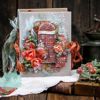 Álbum decorativo com capa em tecido cinza claro e decoração vermelha, ao lado de objetos vintage em madeira e metal