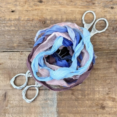 Três tesouras de metal com fita de tecido colorida encima de madeira rústica.