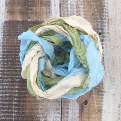 Lenço tecido com cores creme, verde e azul claro enrolado sobre fundo de madeira rústica