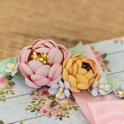 Flores de tecido rosa e amarelo com flores brancas e fita rosa sobre fundo floral