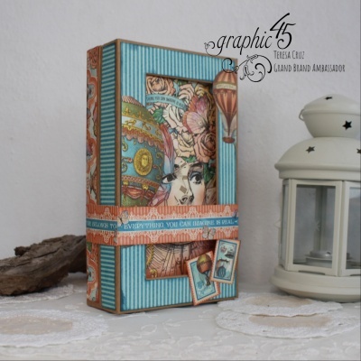 Caixa decorativa azul e bege ilustrada com rosto, globo e flores ao lado de lanterna branca