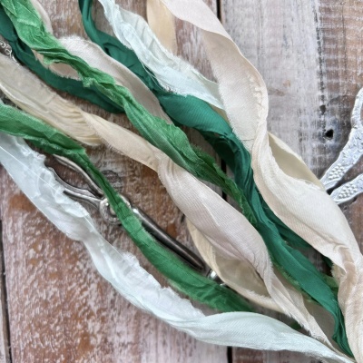 Fios de tecido verde e creme com agulha metálica sobre madeira