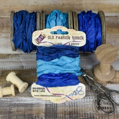 Três fitas azuis em madeira com etiqueta Old Fashion Ribbon sobre mesa rústica com acessórios de costura