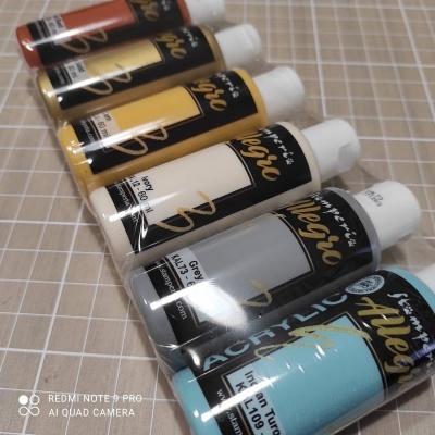 Seis tubos coloridos de tinta acrílica alinhados sobre superfície quadriculada.