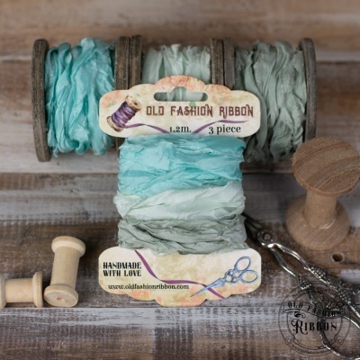 Fitas de tecido azuis enroladas em carretéis de madeira com etiquetas e acessórios sobre mesa de madeira