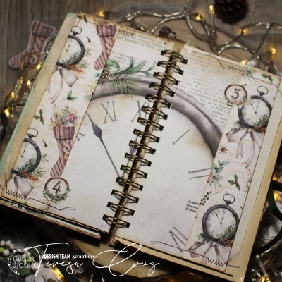 Caderno espiral com decoração vintage de relógios e flores natalícias ao fundo de madeira.