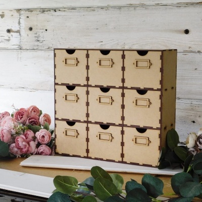 Móvel organizador de madeira com nove gavetas e decoração floral ao redor.