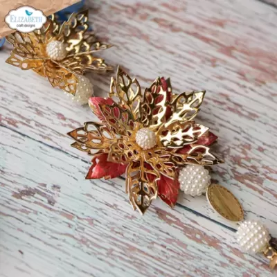 Decoração artesanal com flores metálicas douradas e vermelhas e pérolas brancas sobre madeira pintada.