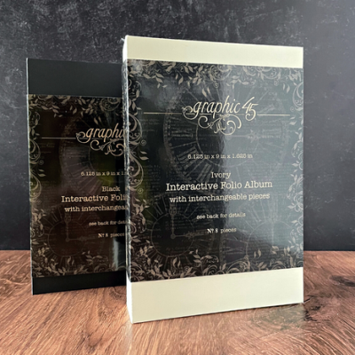 Dois álbuns interativos Graphic 45, preto e marfim, em superfície de madeira