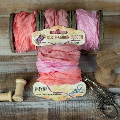 Rolos de fita de tecido rosa com etiquetas OLD FASHION RIBBON dispostos sobre mesa de madeira