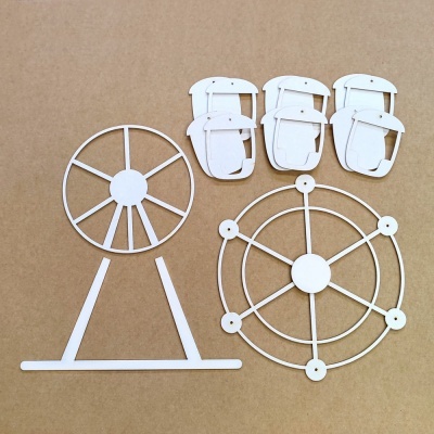 Peças em madeira clara para montar uma roda-gigante sobre superfície castanha