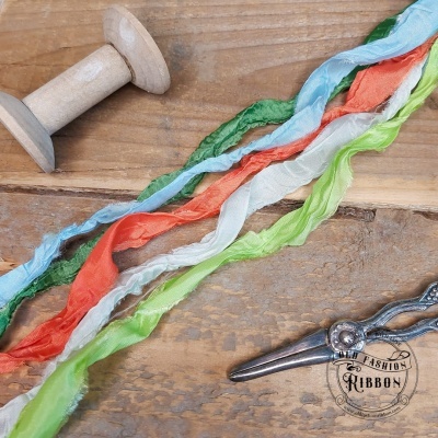 Fitas coloridas, bobina e tesoura sobre madeira com selo 'THE FASHION RIBBON'.