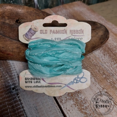 Fita azul-turquesa Old Fashion Ribbon embalada em cartão com ilustrações e texto, sobre mesa de madeira rústica