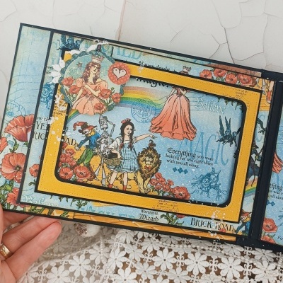 Livro infantil ilustrado aberto com personagens do Mágico de Oz em cores vibrantes.