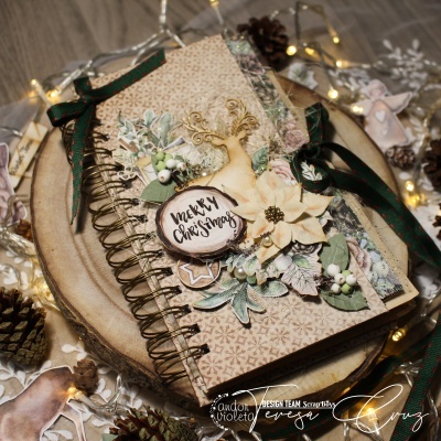 Caderno espiral decorado com tema natalício sobre superfície de madeira com luzes e pinhas