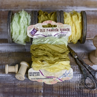 Rolos de fita de tecido verde e amarelo com rótulo old fashion ribbon, carretéis de madeira e tesoura sobre mesa de madeira