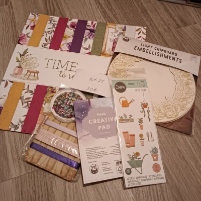 Artigos de papelaria e artesanato com papéis decorativos e etiquetas com textos em embalagem sobre chão de madeira.