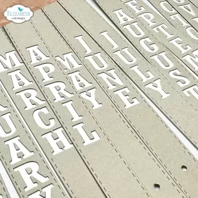 Tiras de papel cinzento com letras brancas recortadas formando nomes, sobre fundo de madeira clara.