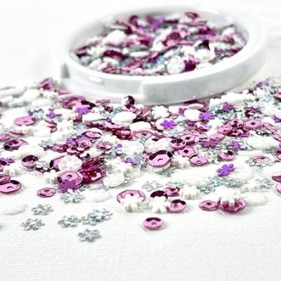 Sequins coloridos rosa, prateado e roxo variados em superfície branca com recipiente branco