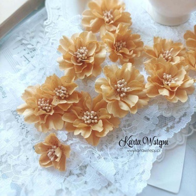 Flores decorativas bege em tecido sobre renda branca e papel com texto.