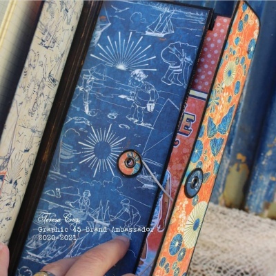 Quatro agendas ou cadernos com diferentes padrões nas capas e fechos, empilhados sobre uma superfície clara.