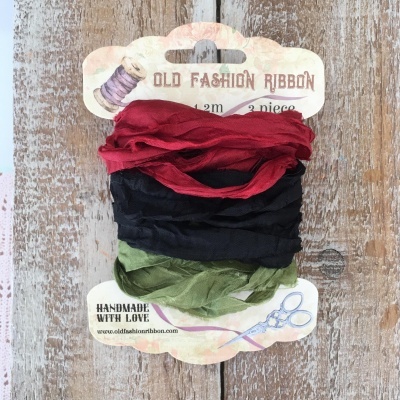 Fitas antigas de tecido vermelho, preto e verde com textura enrugada em embalagem de cartão