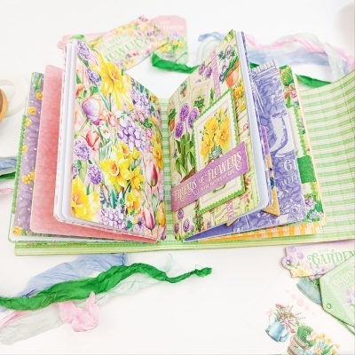 Álbum decorativo aberto com ilustrações florais e fitas coloridas ao redor