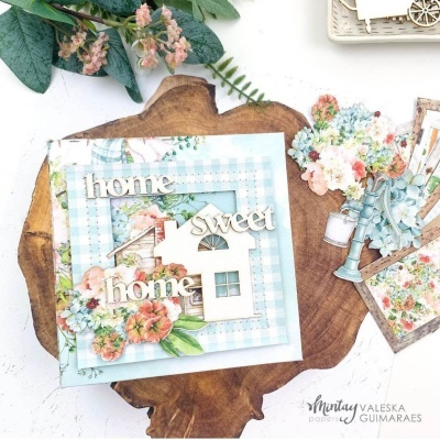 Peça decorativa azul claro com casa em relevo, palavras em madeira e flores sobre base de madeira