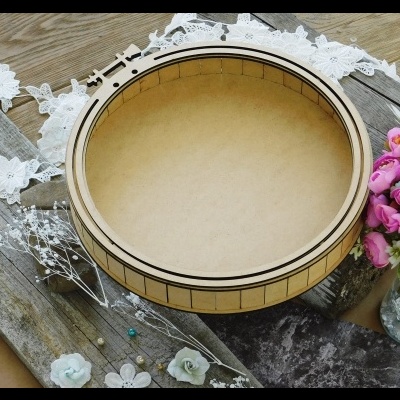 Cesto redondo de madeira clara com decoração riscada sobre fundo rústico e flores coloridas