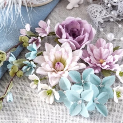 Arranjo floral artificial com flores lilás, branco e azul claro sobre tecido e rendas
