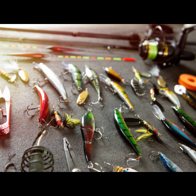 Coleção variada de iscos de pesca coloridos organizados numa superfície preta com bobina de linha de pesca ao fundo.