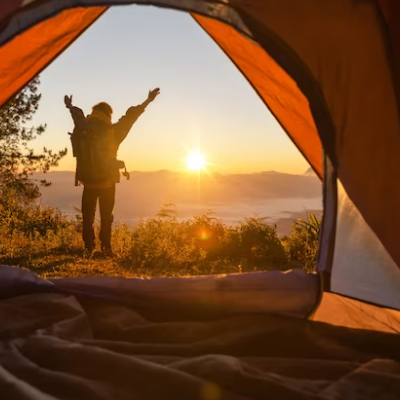 Interior de tenda a enquadrar pessoa com mochila ao pôr do sol