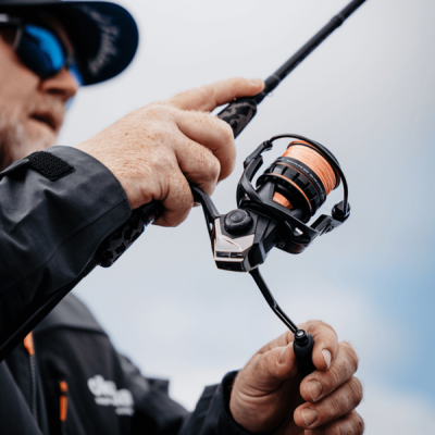 Pessoa segurando cana de pesca com molinete preto e linha laranja