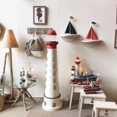 Decoração náutica com farol, barcos em miniatura, candeeiro de corda e quadros com temas marítimos