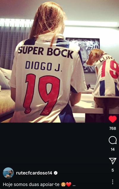 Duas camisolas de futebol brancas com nomes e números iguais, usadas por pessoa e cão dentro de casa.