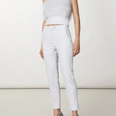 Conjunto branco feminino com top de franjas e calças justas, usando sapatos de salto xadrez.