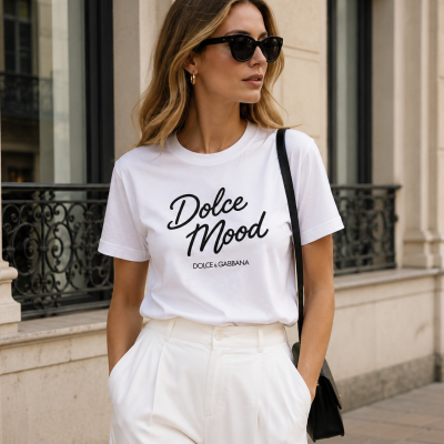 Woman wearing white Dolce Mood T-shirt with white pants and black sunglasses outdoors.
