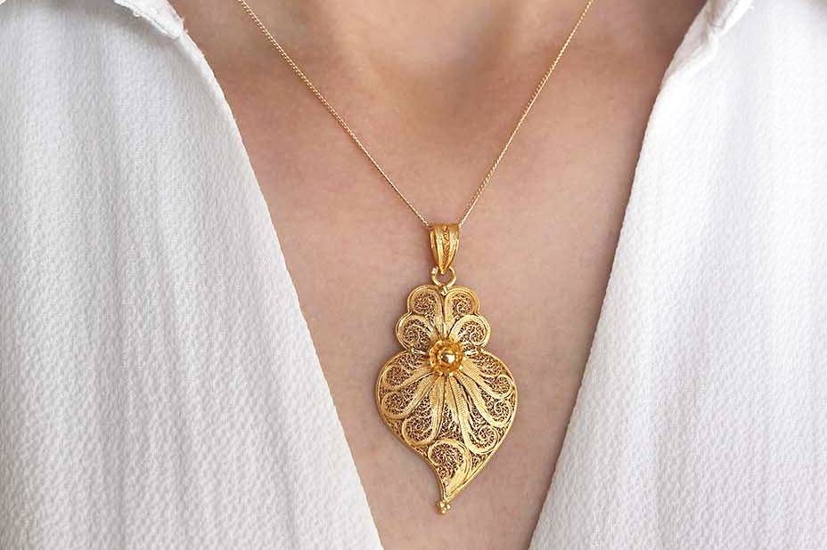 Colar dourado com pendente em forma de folha e flor central no pescoço