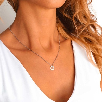 Colar prateado com pendente redondo vazado em forma de quatro folhas, usado por mulher com blusa branca.