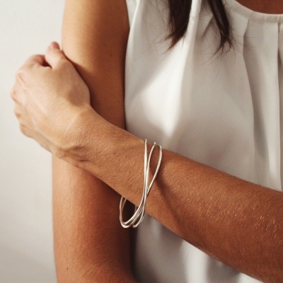 Pulseira prateada entrelaçada no braço de mulher com blusa branca