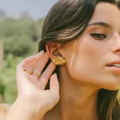 Mulher a usar brincos dourados com textura floral e a tocar no brinco