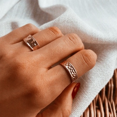 Mão com dois anéis de prata em fundo de tecido branco e vime