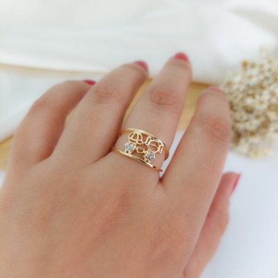 Anel dourado com pedras transparentes numa mão feminina com unhas vermelhas