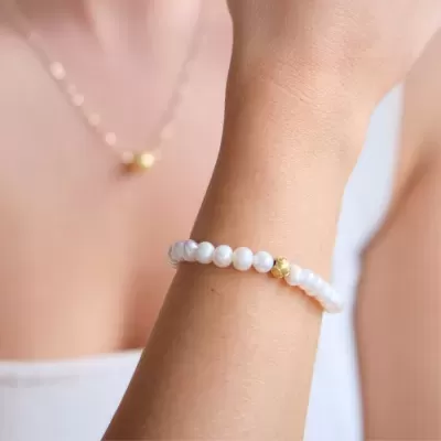 Pulseira feminina de pérolas brancas com detalhe dourado no pulso.