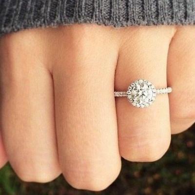 Anel prateado com pedra central brilhante na mão com roupa cinzenta