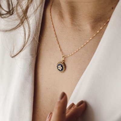Colar dourado com pendente azul com flor branca no centro