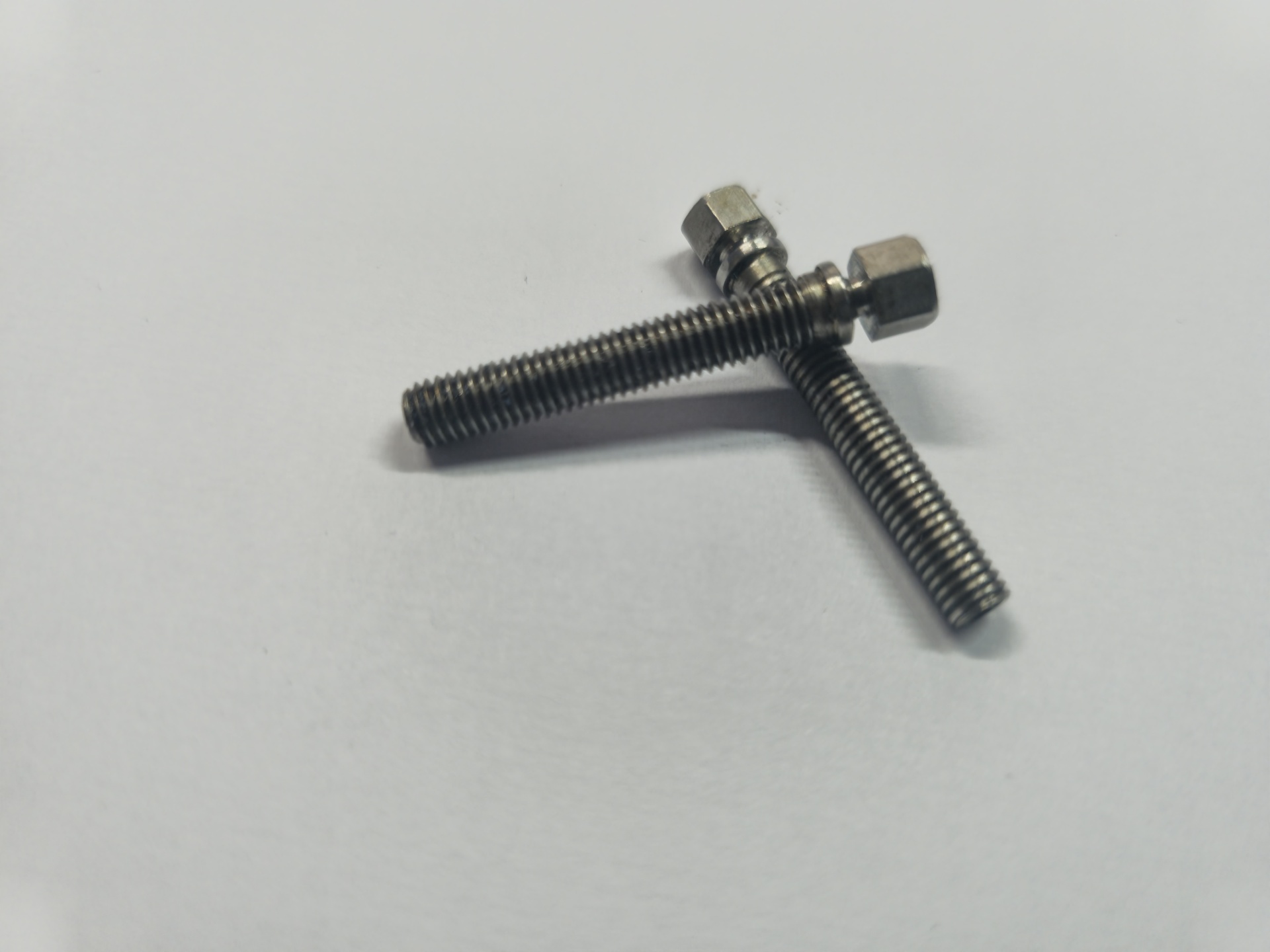 Dois parafusos metálicos prateados com cabeça sextavada sobre superfície branca